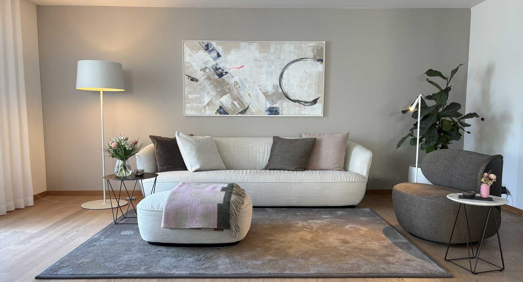 Wohnzimmer in Walchwil mit hellem Sofa, Sessel und abstraktem Bild an graubeiger Wand